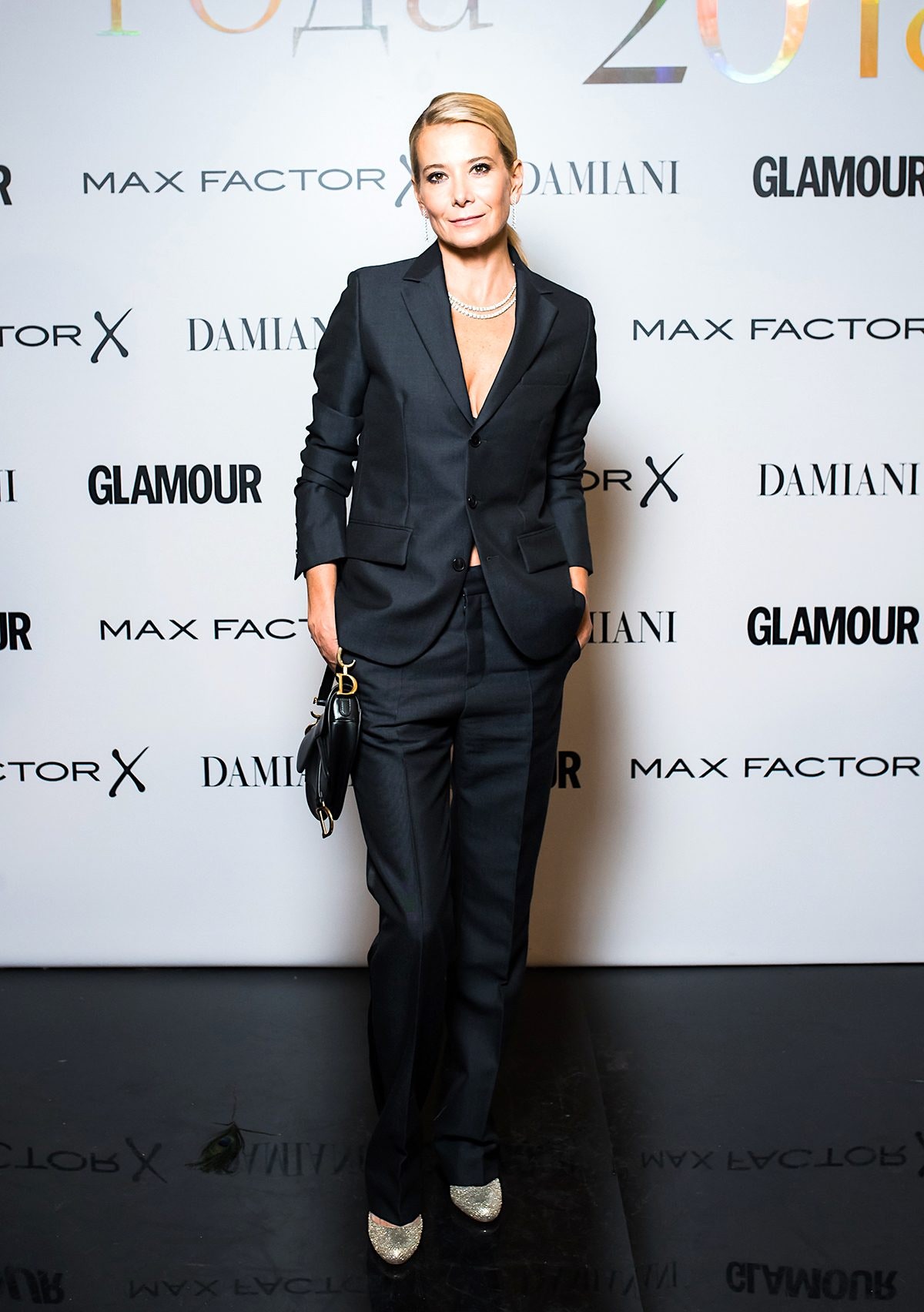 Юлия Высоцкая выбрала классический черный костюм с глубоким декольте который она дополнила сумкой Dior.