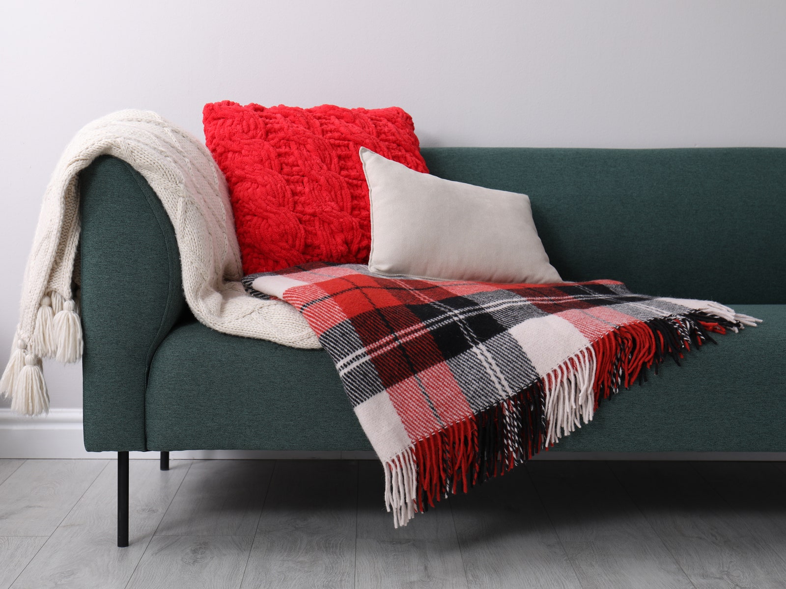 Sofa with soft pillows and warm plaids near light wall indoors