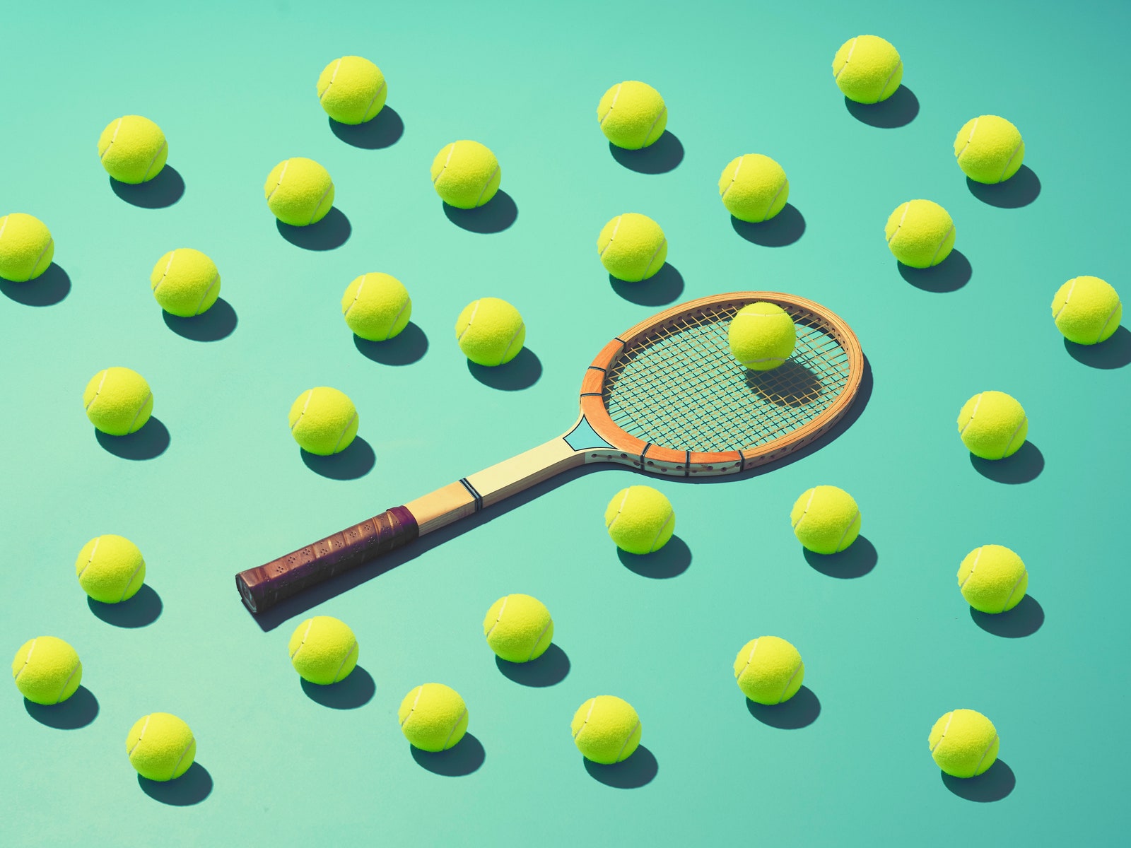 A tennis racket surrounded with a large number of tennis balls