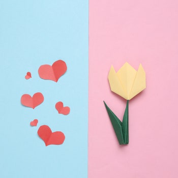Handmade origami paper tulip and paper cut heartsnon pink blue background. 8 March or mother's day concept. Top view....