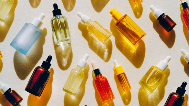 Set of many different glass bottles with cosmetic liquids on white surface. Play of light creates abstract patterns from...